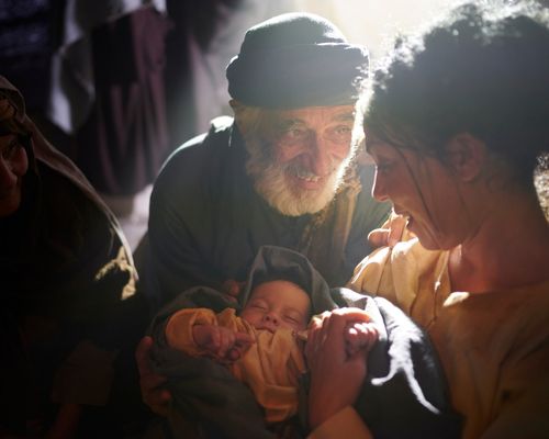Elderly man smiling at young woman holding newborn baby